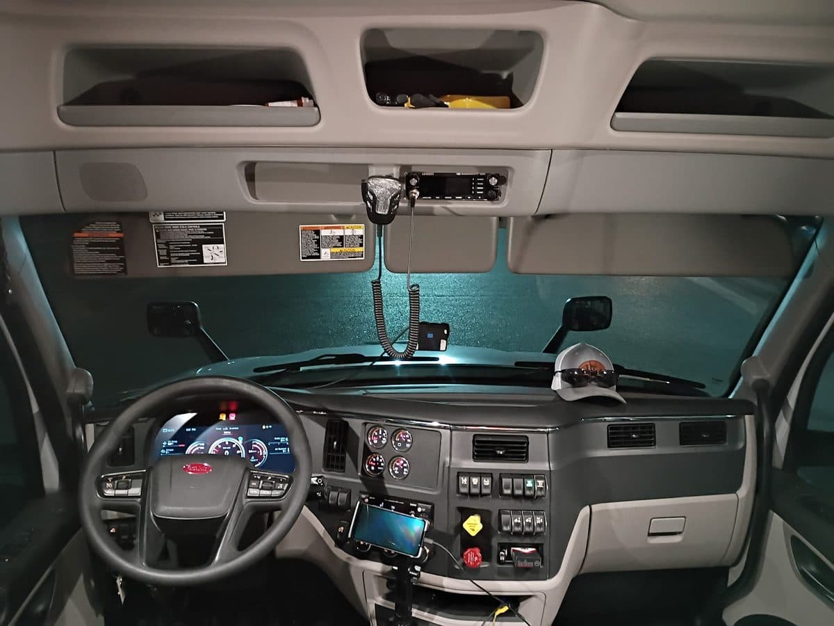The interior of a truck cab at night — steering wheel, digital gauge cluster, CB radio and dash switches.