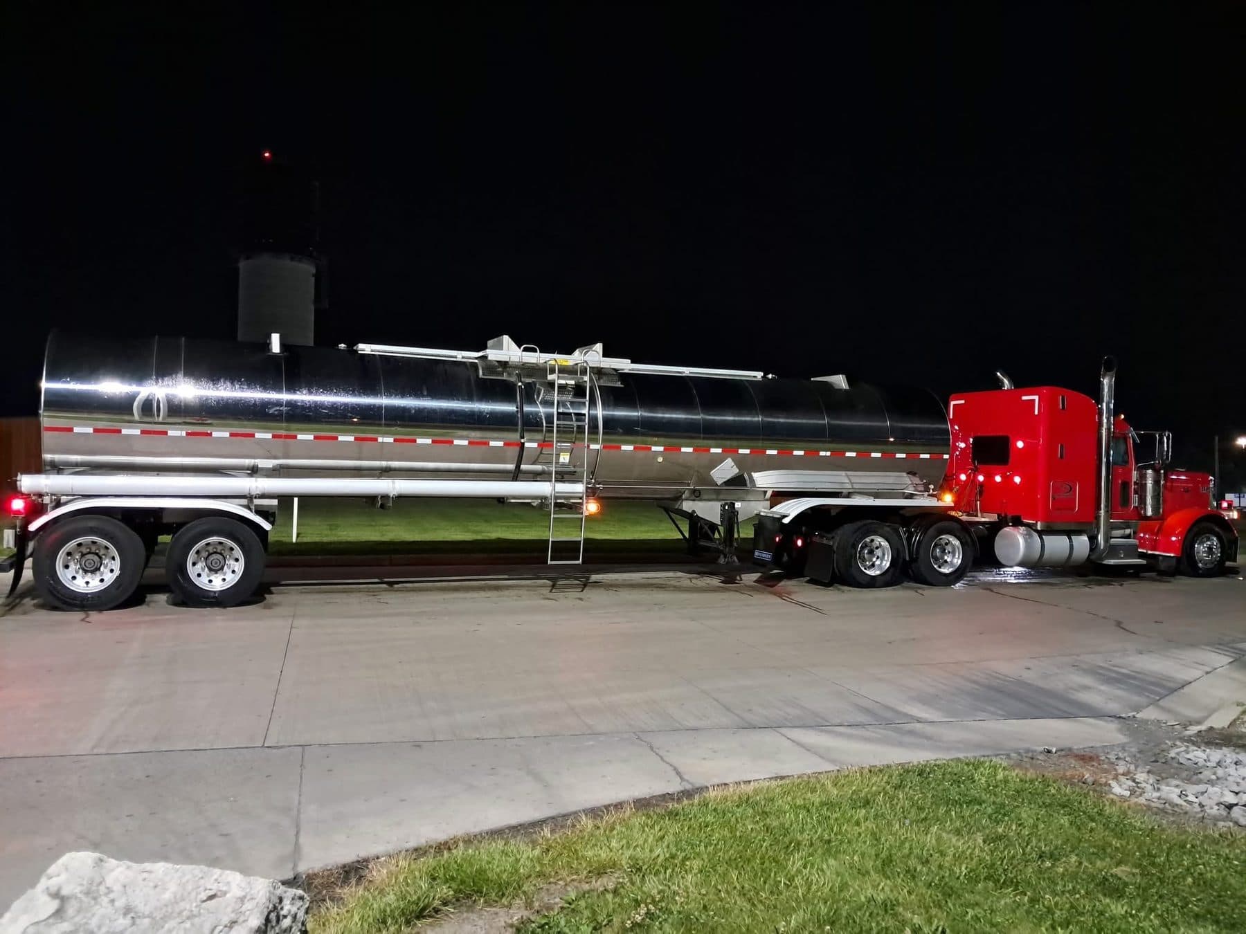 A red Peterbilt 389 coupled to a polished stainless tanker trailer, parked at night.