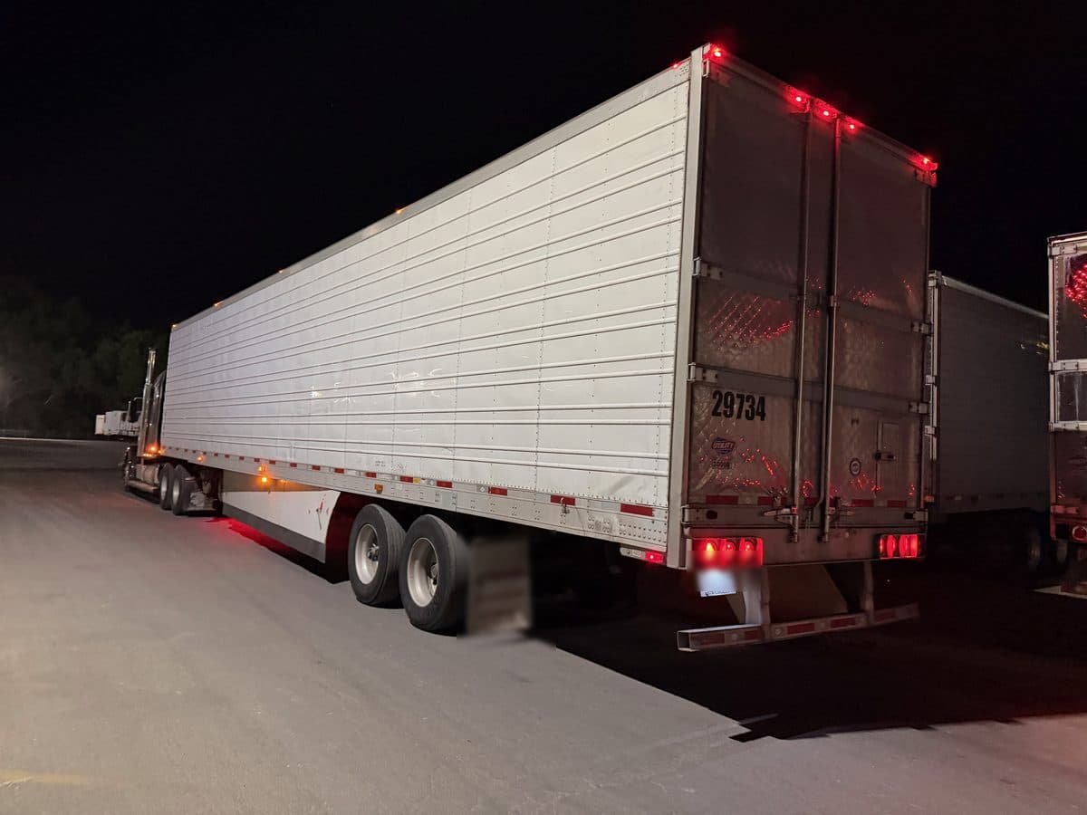The rear of a refrigerated trailer at night in a truck stop lot, marker lights glowing red.